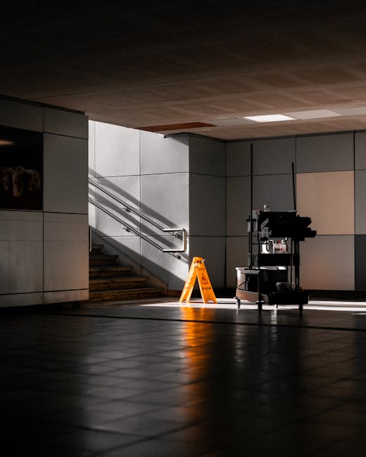 An indoor commercial space featuring a tiled floor with a reflective, clean surface illuminated by natural light coming from the right side. The background includes a staircase with metal handrails le